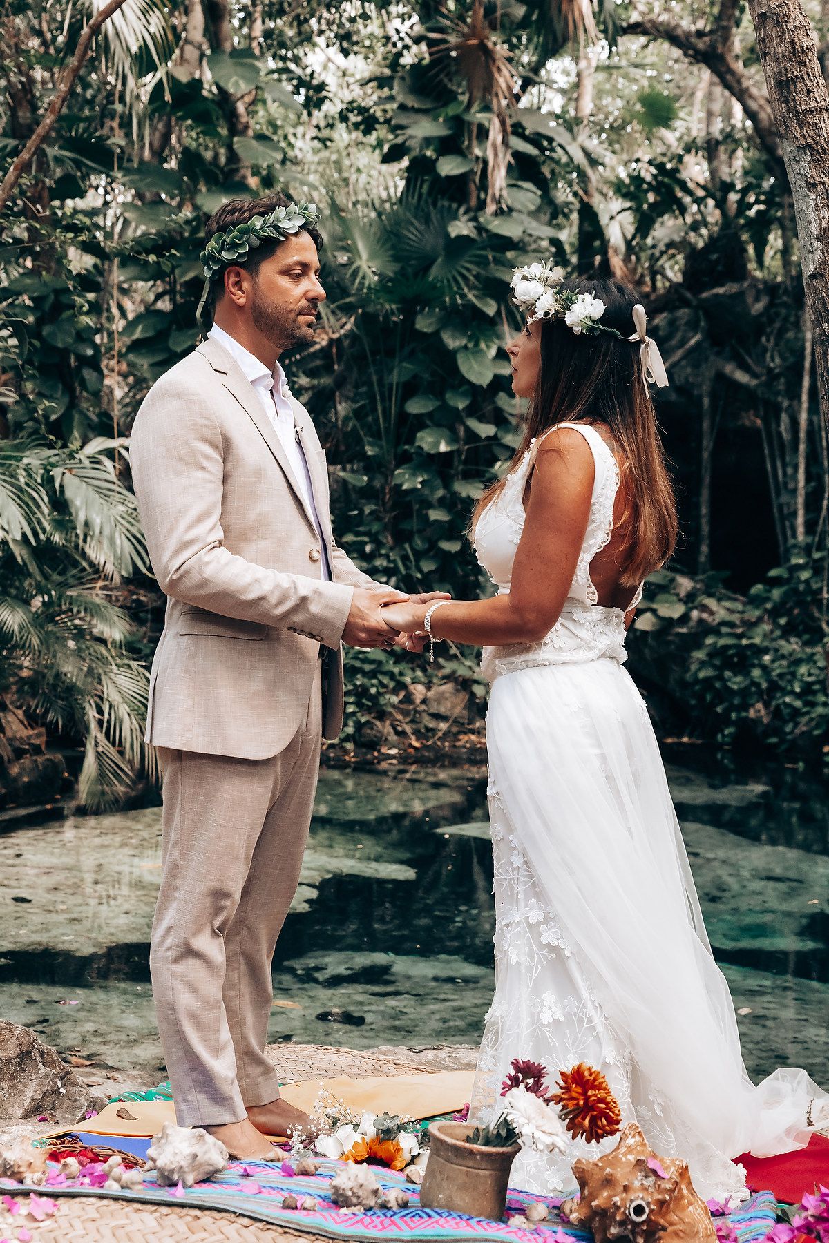A couple performs a traditional wedding ceremony ritual on a colorful blanket in a lush garden setting.