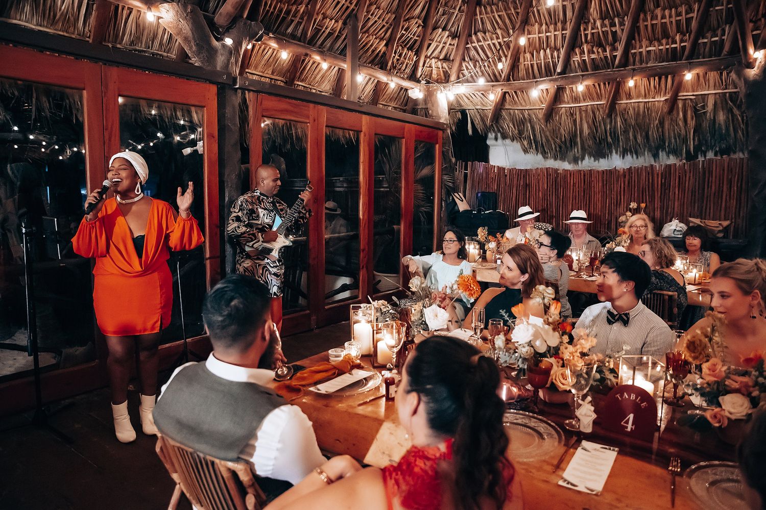 Wedding reception under thatched roof palapa with string lights creating warm ambiance.