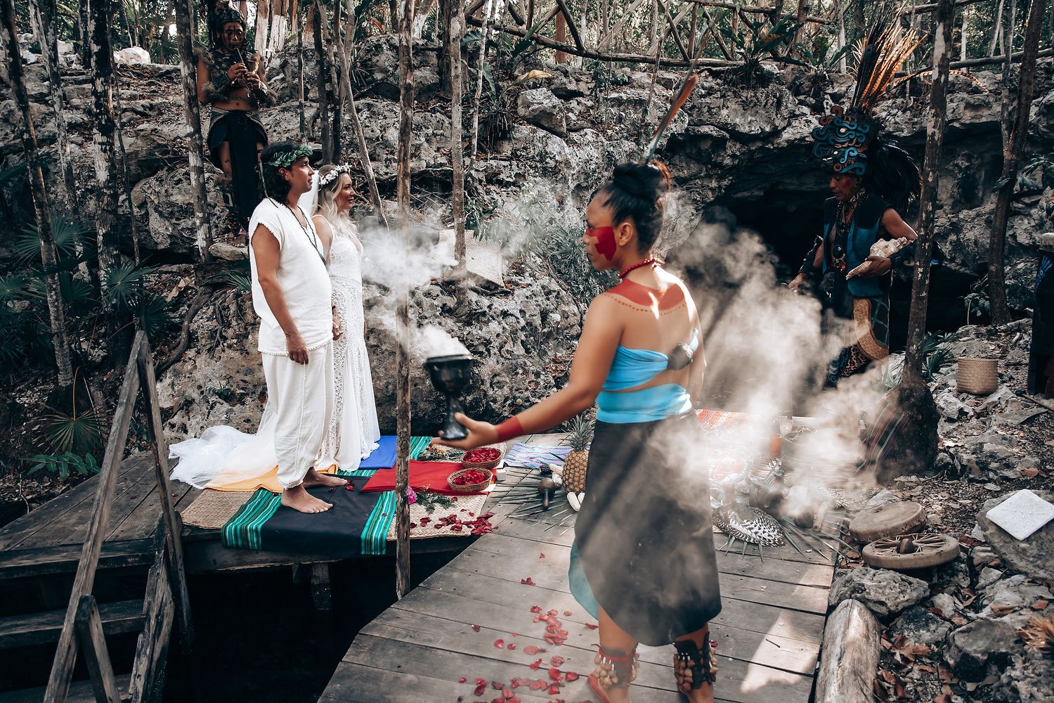 People prepare traditional food in an outdoor cooking area with smoke rising from multiple cooking stations.