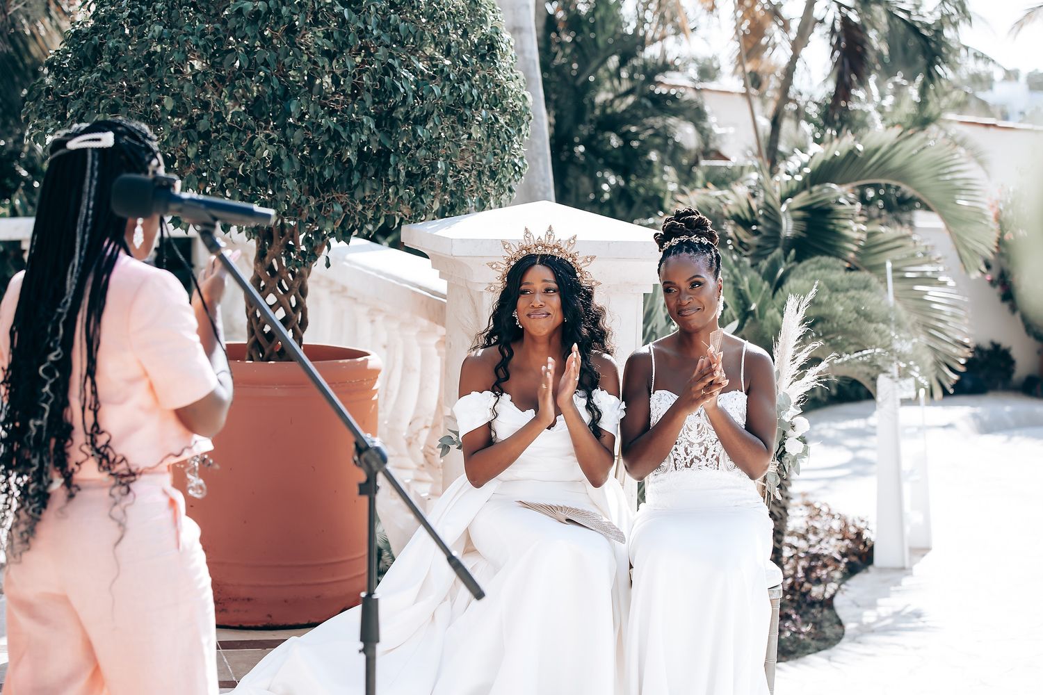 Wedding celebration scene with guests dancing outdoors under palm trees and white decor.
