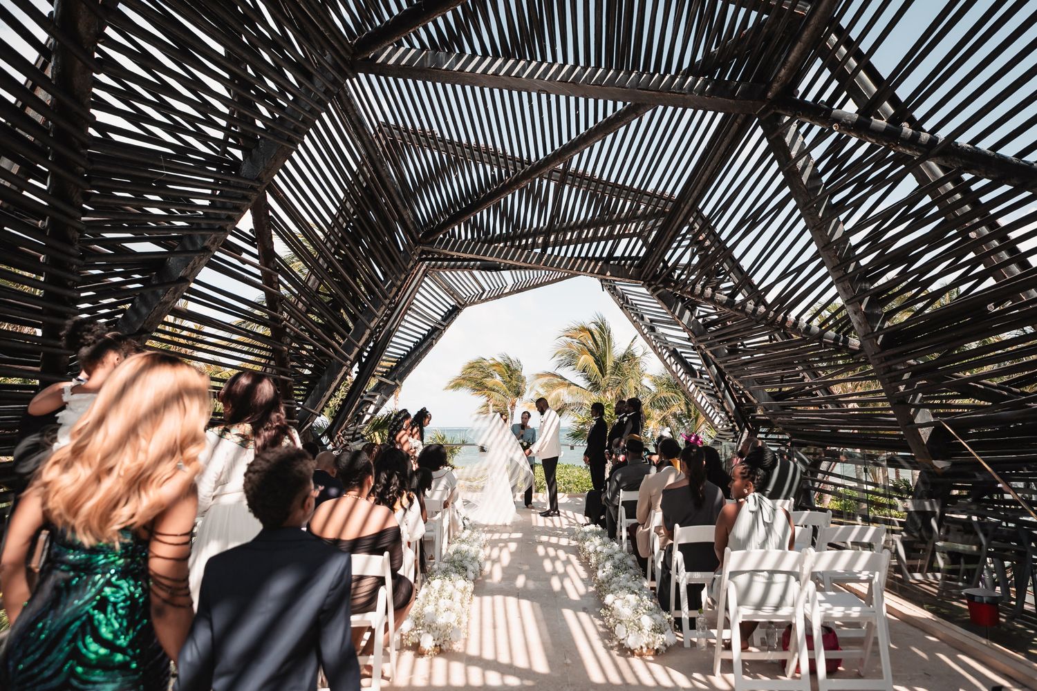 Wedding ceremony under rustic wooden pergola structure with ocean view in background.