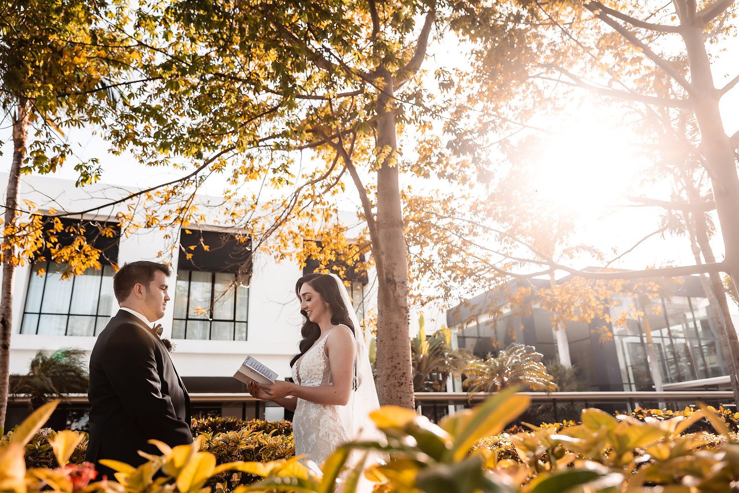 Couple exchanging vows outdoors under golden autumn trees with warm sunlight glowing behind them.
