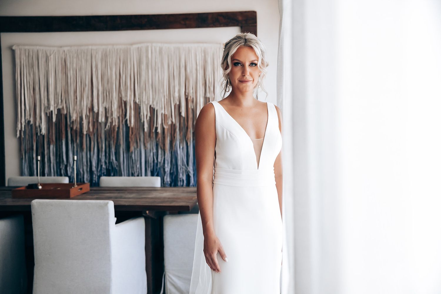 Bridal party in white and cream dresses posing together in bright interior space.