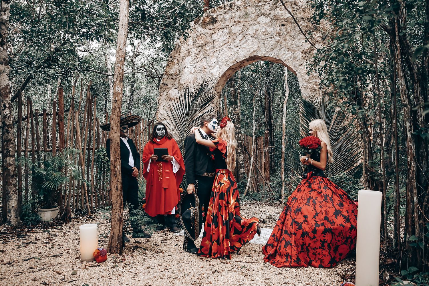 Stone archway decorated with red flowers for gothic-themed outdoor wedding.