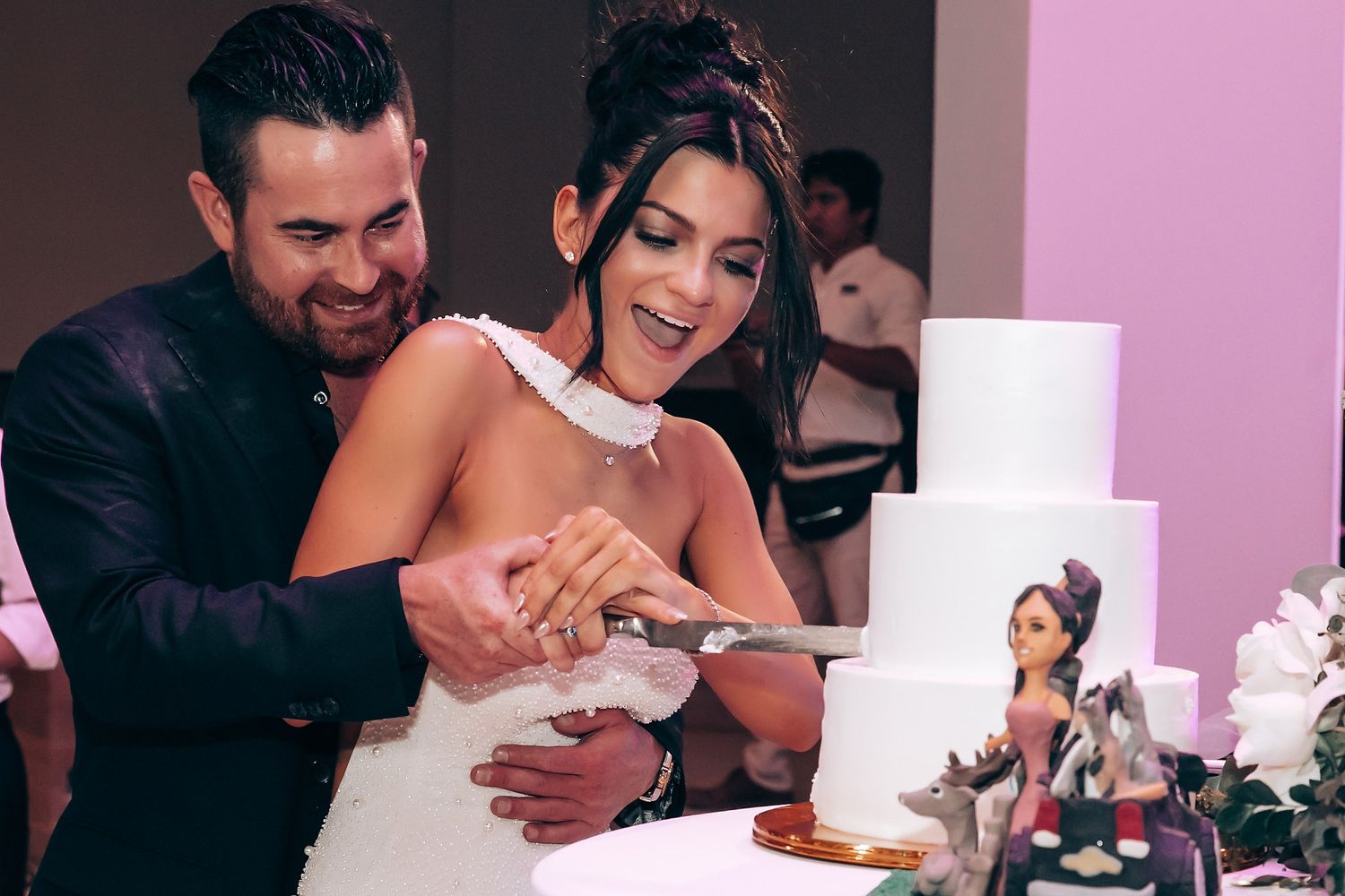 Wedding celebration with pink lighting and white decor elements in modern indoor space.