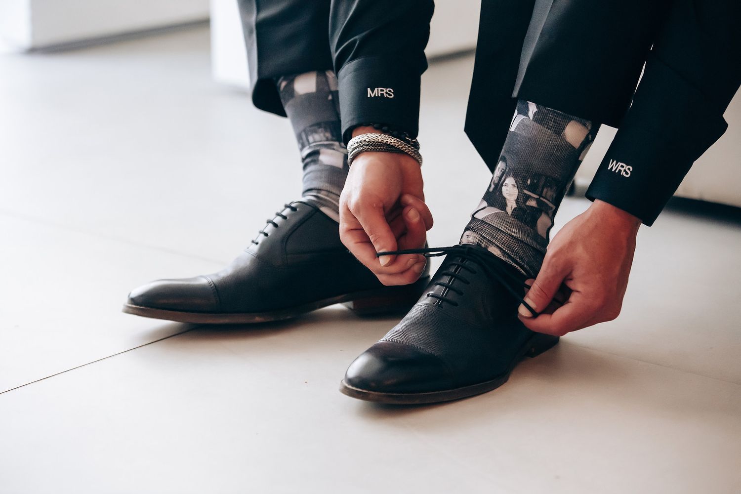 Close-up view of formal black dress shoes being tied on a white floor.