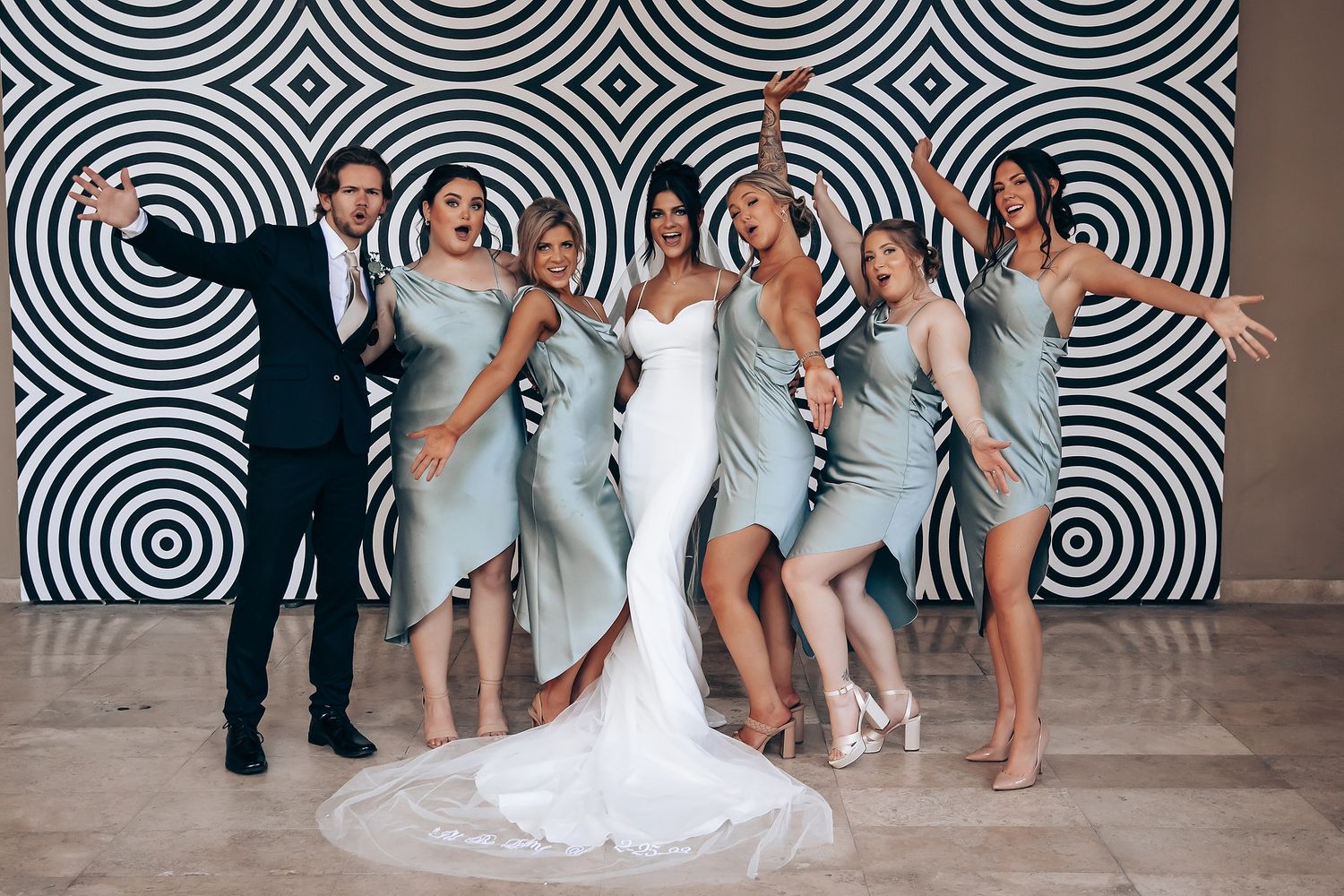 Wedding party poses playfully in front of black and white spiral backdrop at reception venue.