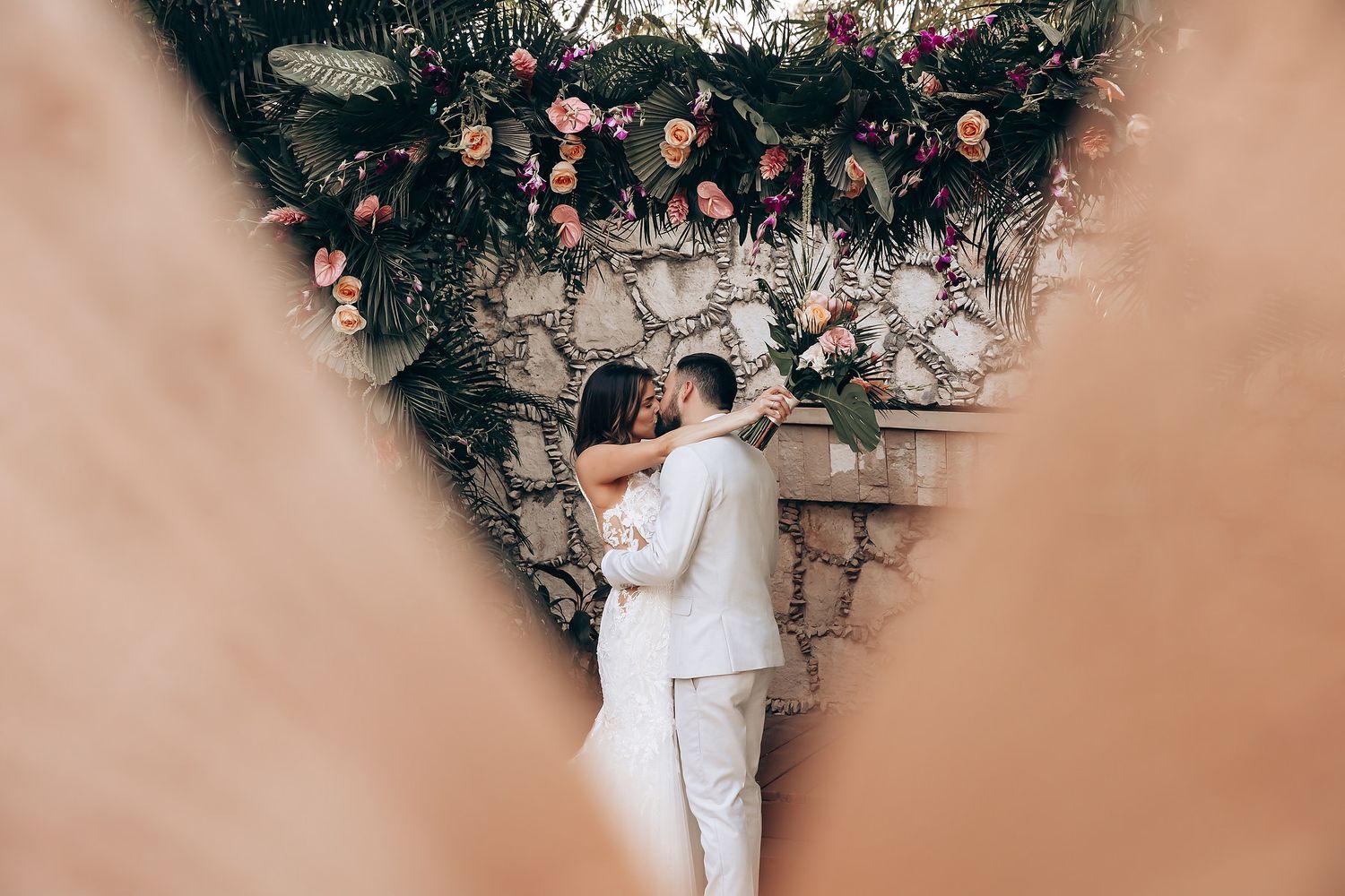 Romantic moment against stone wall decorated with hanging flowers and vines.