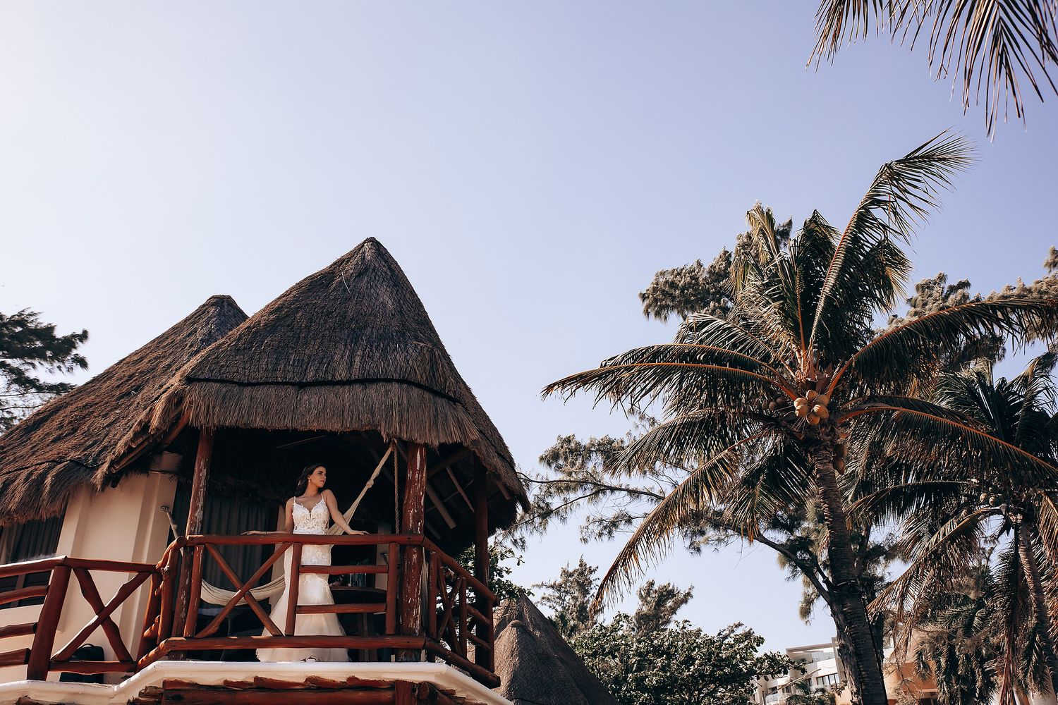 Tropical beach resort with thatched-roof bungalows and palm trees at sunset.