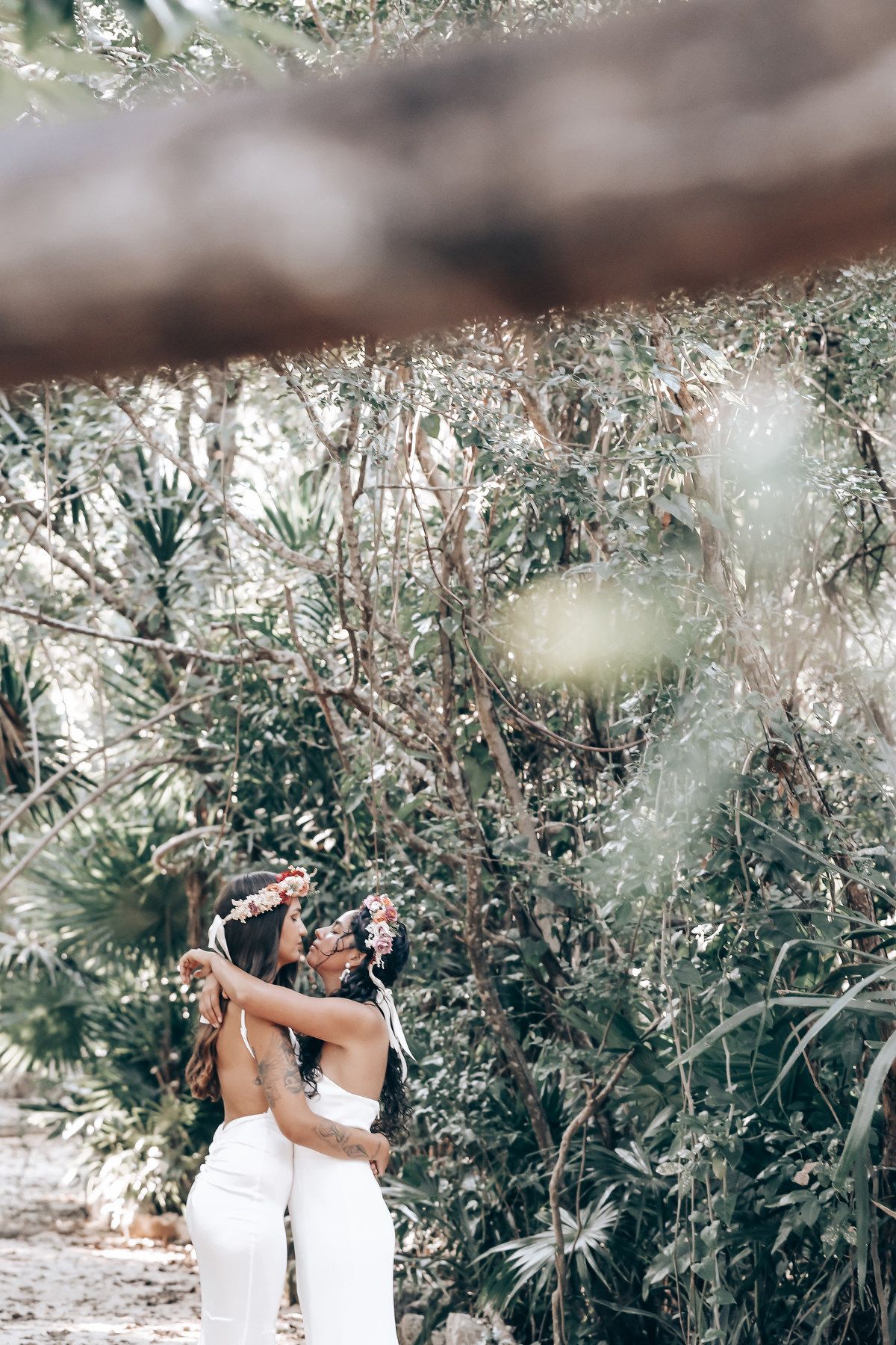 Two people embrace in a romantic moment surrounded by lush tropical vegetation.