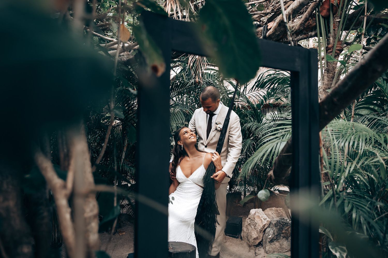 Artistic wedding photography through tropical foliage at beach ceremony.