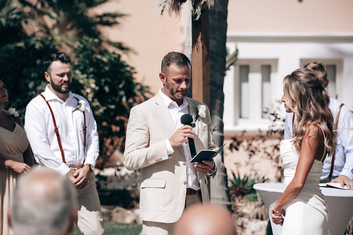 A wedding ceremony with a groom speaking to a bride and guests in the background.