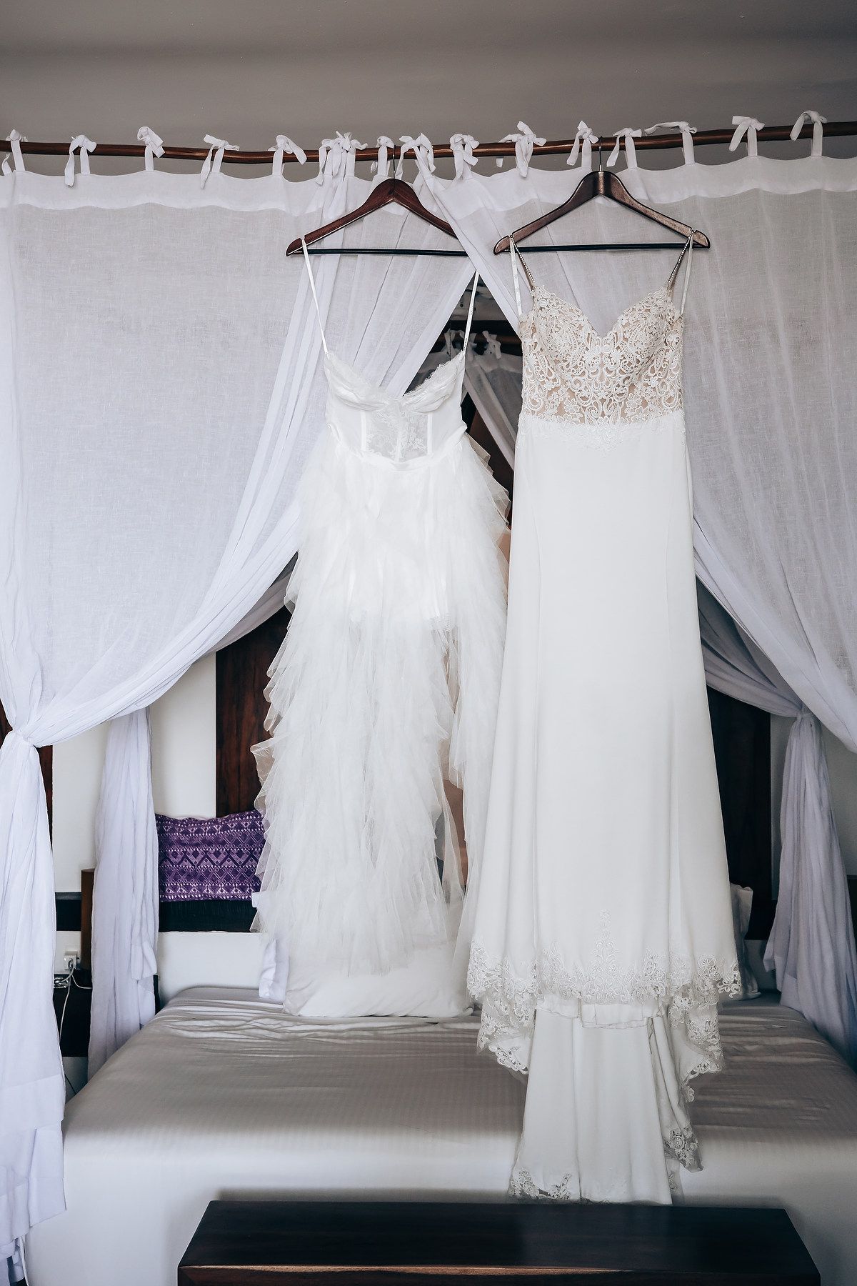 Image of two white wedding dresses hanging on a rack with a sheer curtain backdrop.