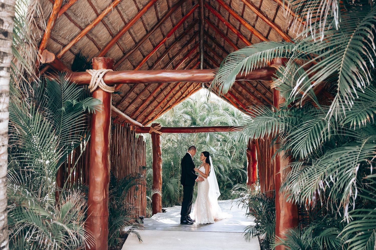A wedding ceremony under a wooden pergola surrounded by tropical foliage.