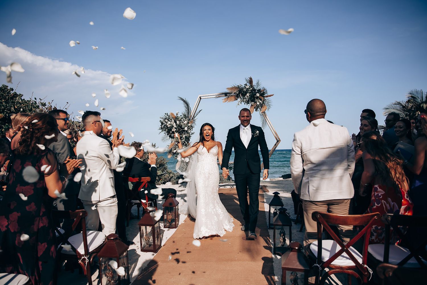 Rose petals being tossed in the air during an outdoor beach wedding celebration.