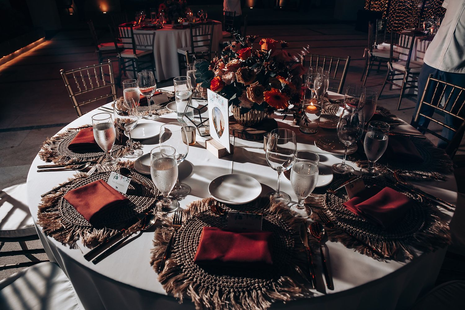 Elegant wedding reception table setting with formal place settings and red floral centerpieces.