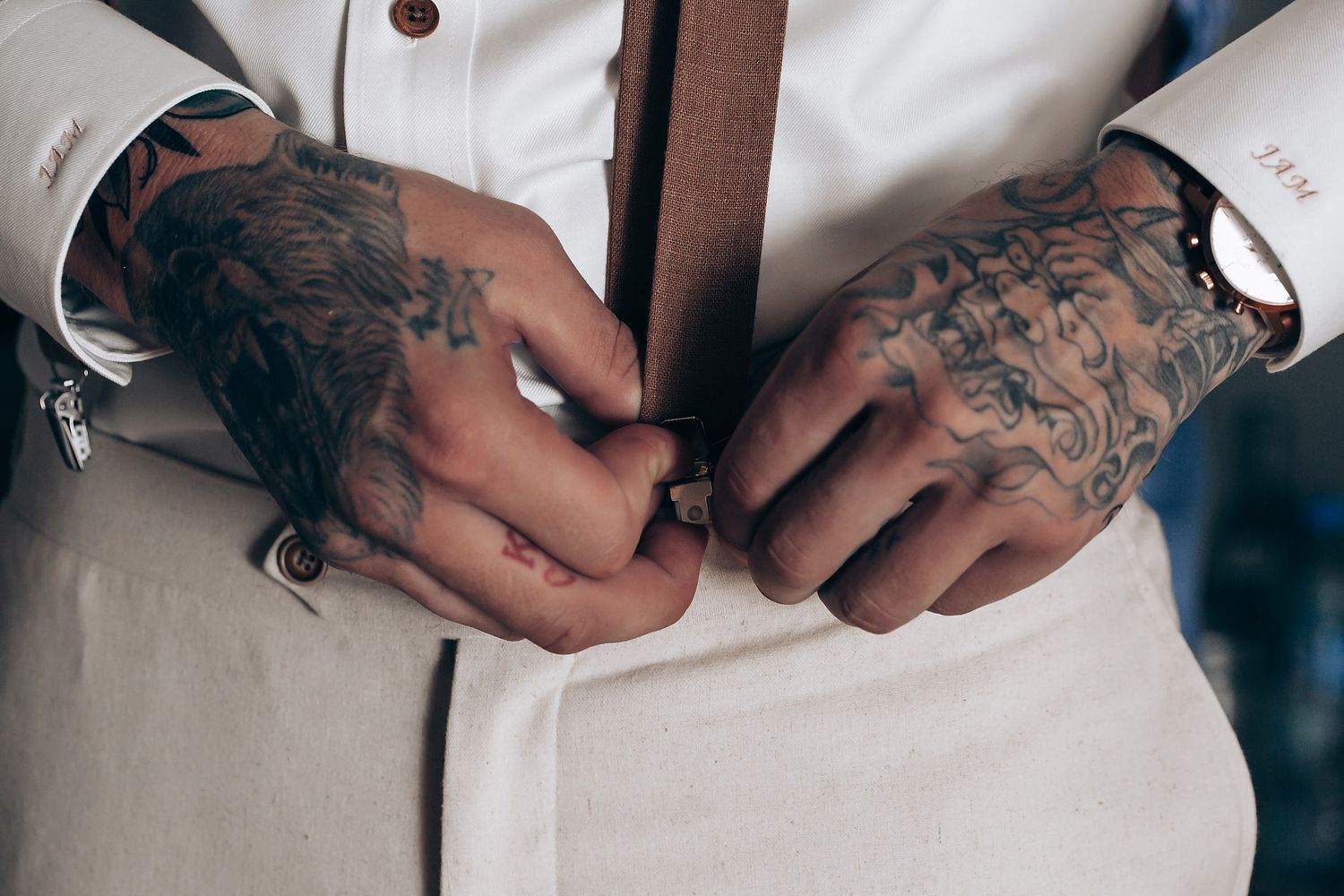 Close-up of tattooed hands adjusting formal white attire.