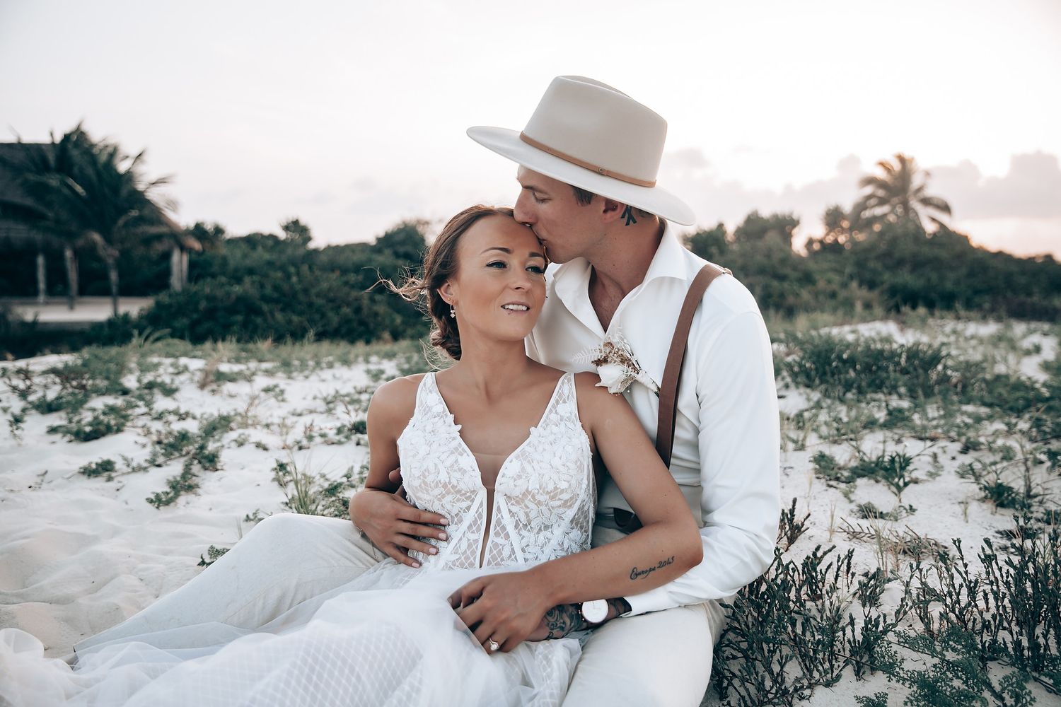 A romantic beach wedding photoshoot at sunset with coastal vegetation in the background.