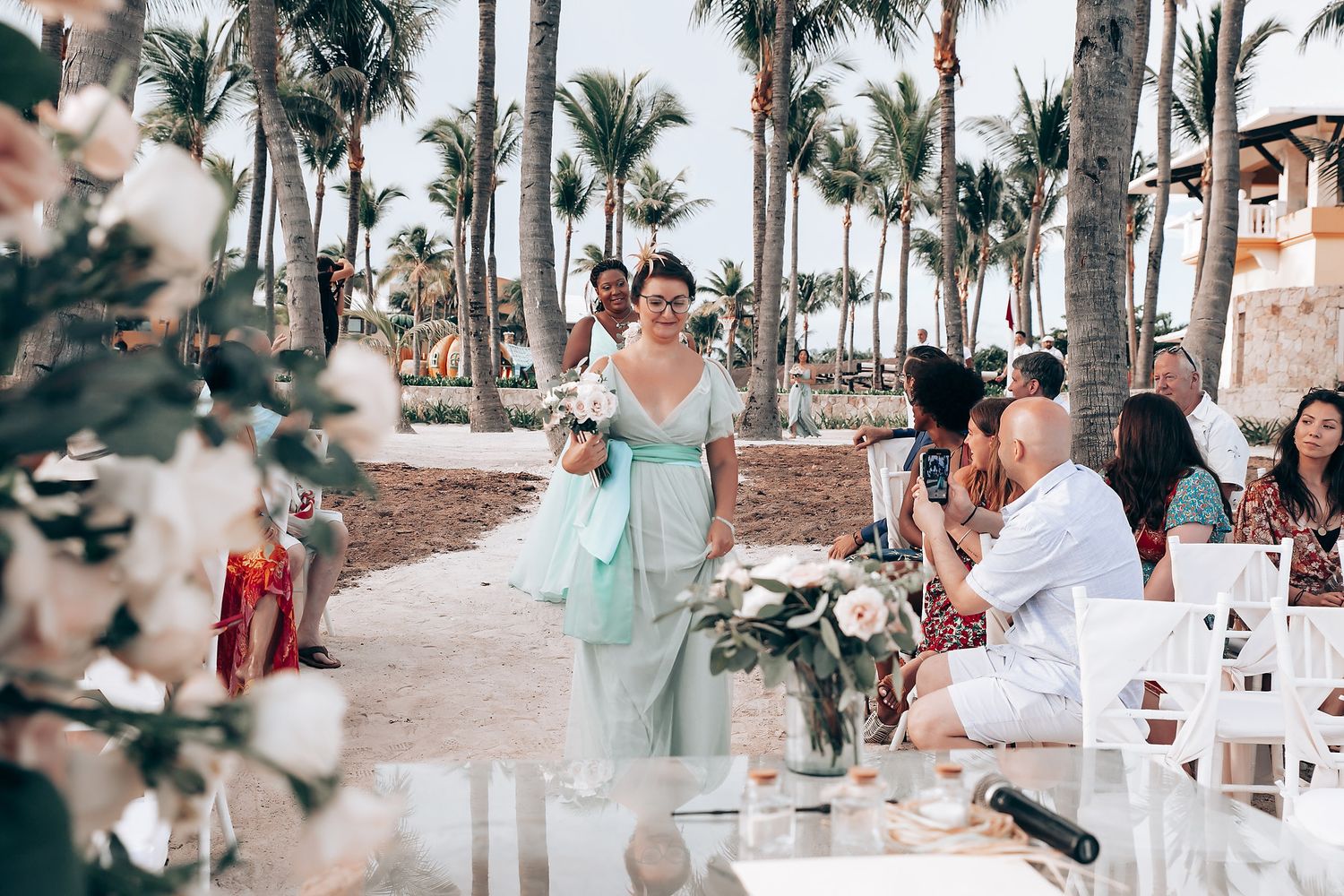 Tropical beach wedding reception setup with palm trees and white decor.