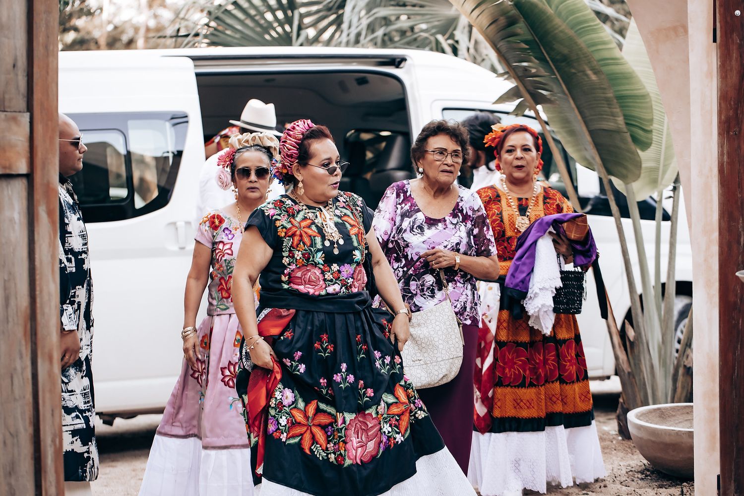 Festive outdoor gathering with colorful traditional dress and decorations under palm trees.