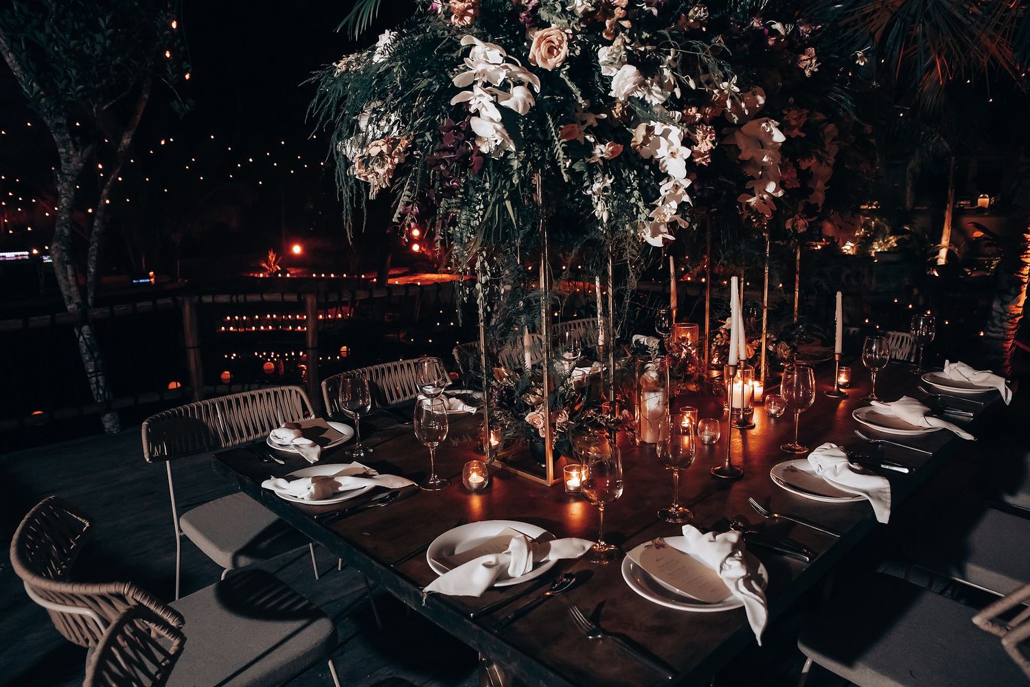 An elegant table setting with candles and floral arrangements under a dark, moody ambiance.