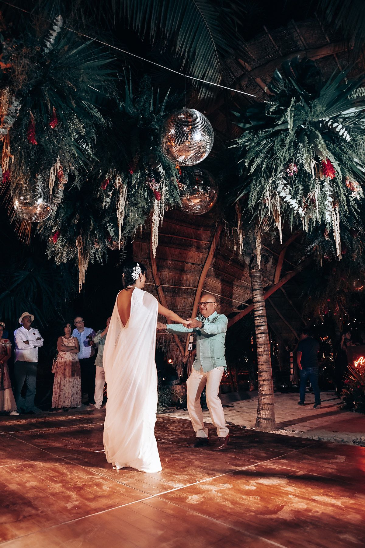 Wedding couple's first dance under palm trees with disco ball and ambient lighting.