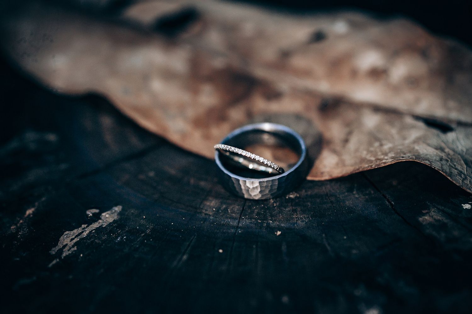 Close-up of wedding rings on dark textured surface with artistic bokeh lighting effects.
