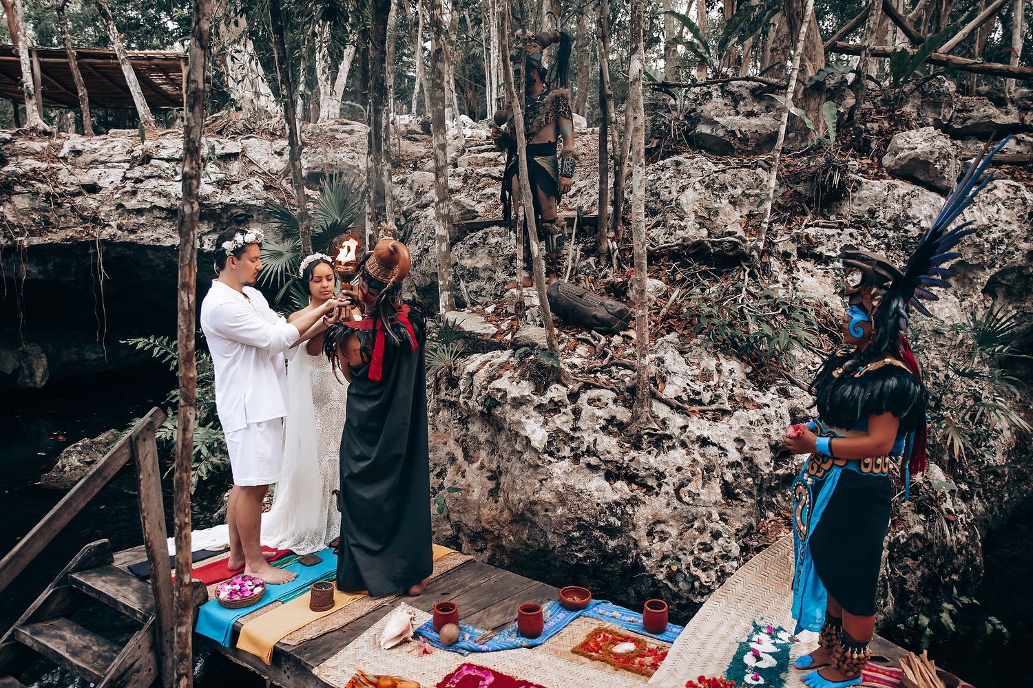 A group of people enjoying a winter picnic in a snowy forest with blankets and food spread out on the ground.