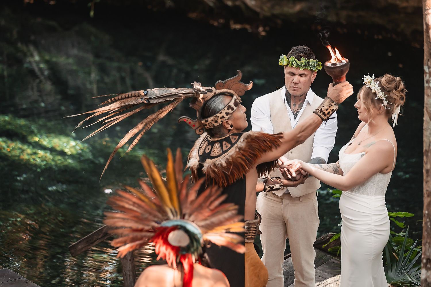 Couple exchanges vows in Mayan ceremony with shaman holding torch near cenote in Mexico.