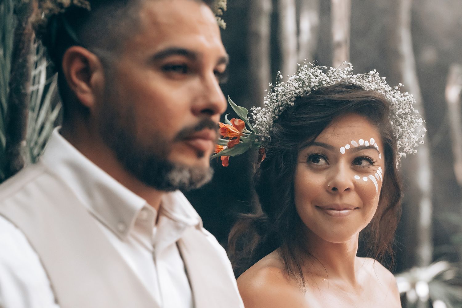 Couple in wedding attire standing close together in a misty forest setting.