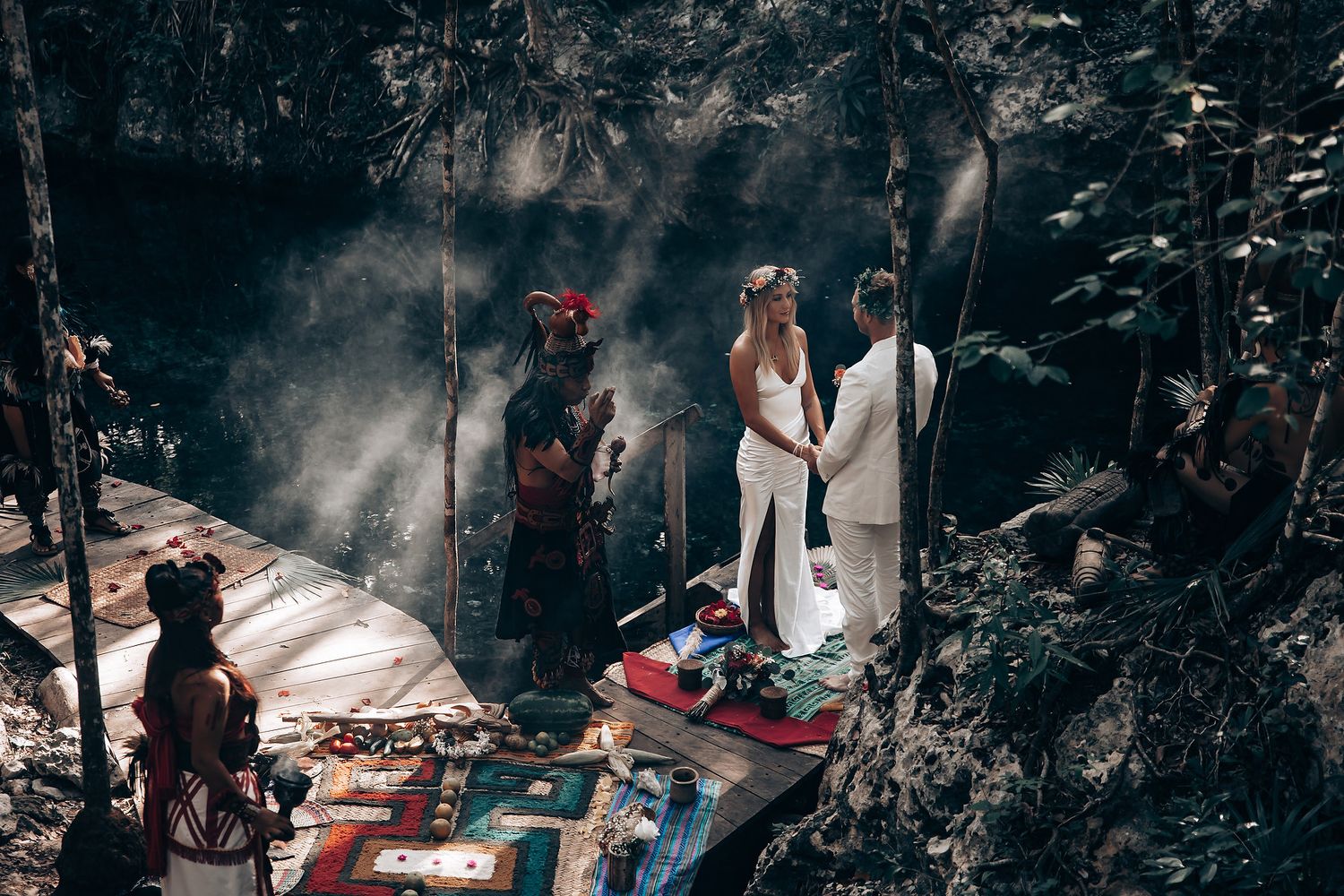 An intimate forest wedding ceremony unfolds with guests gathered among tall trees.