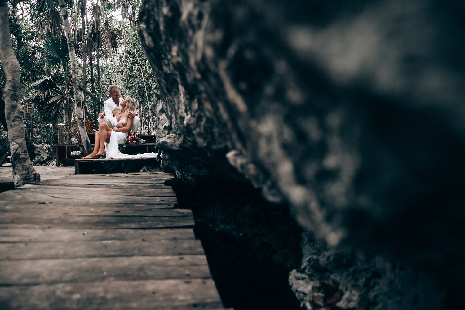 A rustic wooden walkway leads through a dimly lit forest wedding venue.
