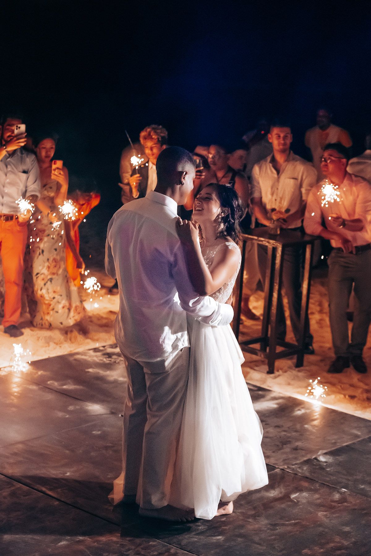 Couple sharing a romantic dance surrounded by sparklers at nighttime wedding celebration.