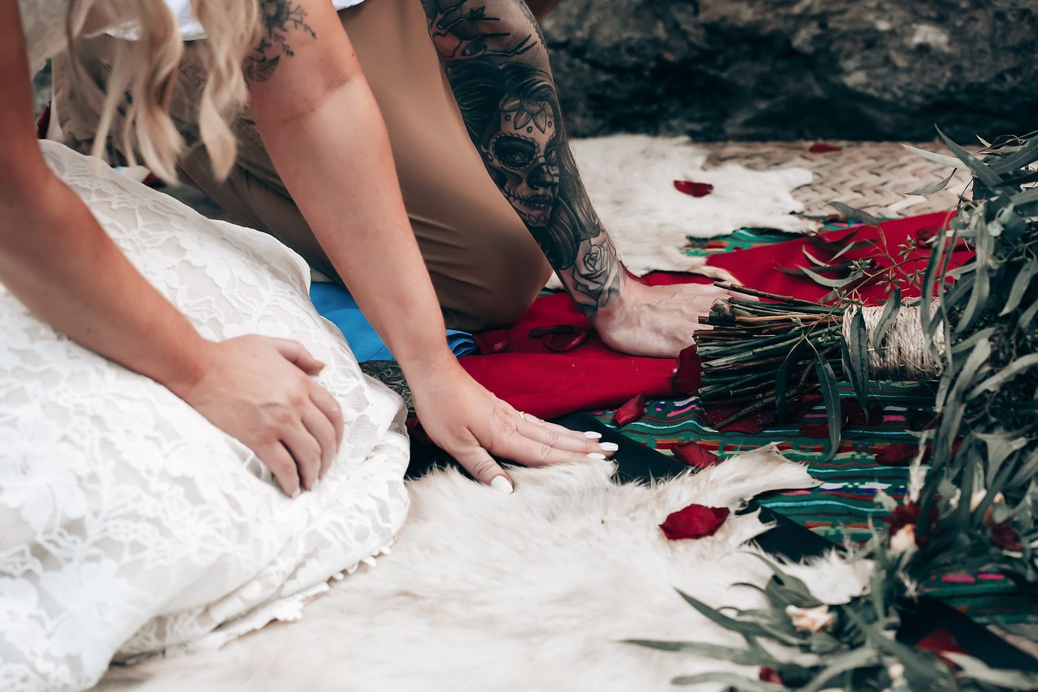 Decorative ceremony setup with red rose petals and white fabric on natural stone surface.