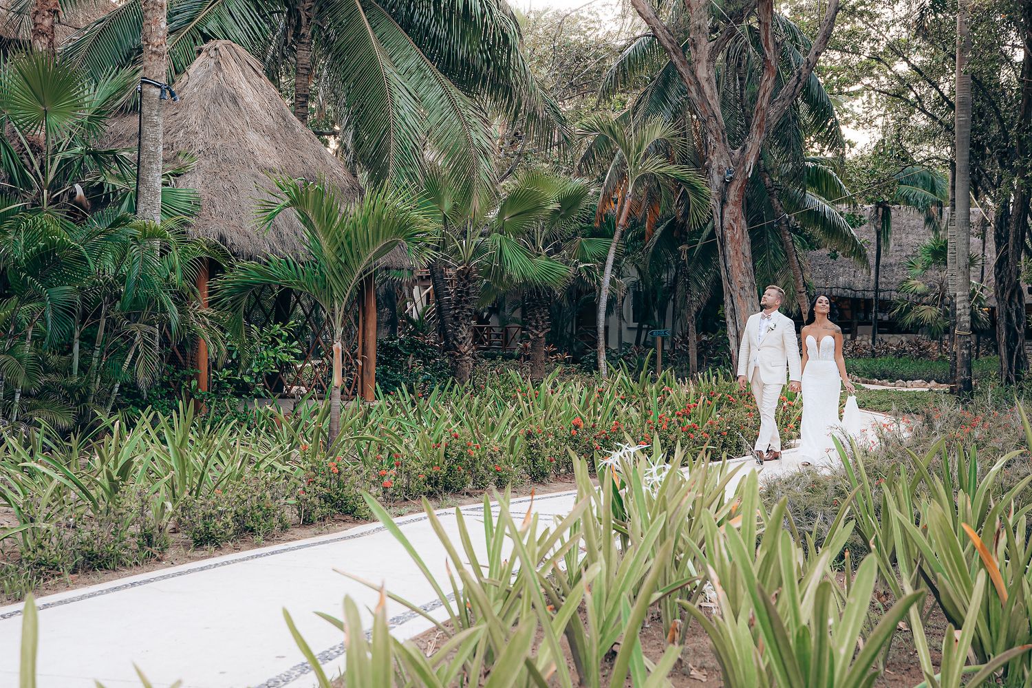 Wedding couple strolling through a lush garden landscape with palm trees and tropical foliage.