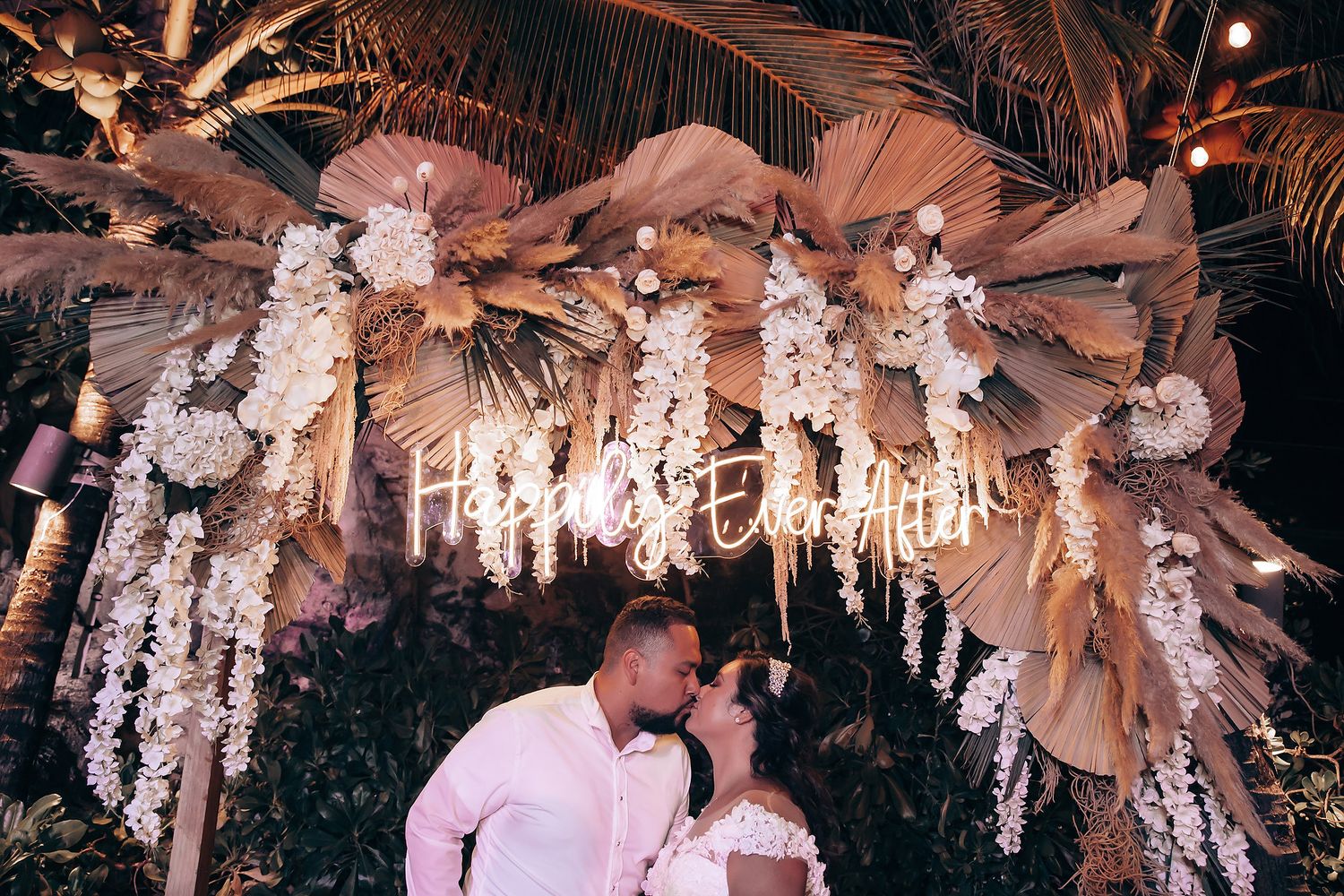 Ornate white floral arrangements and chandeliers decorate a romantic wedding reception ceiling.