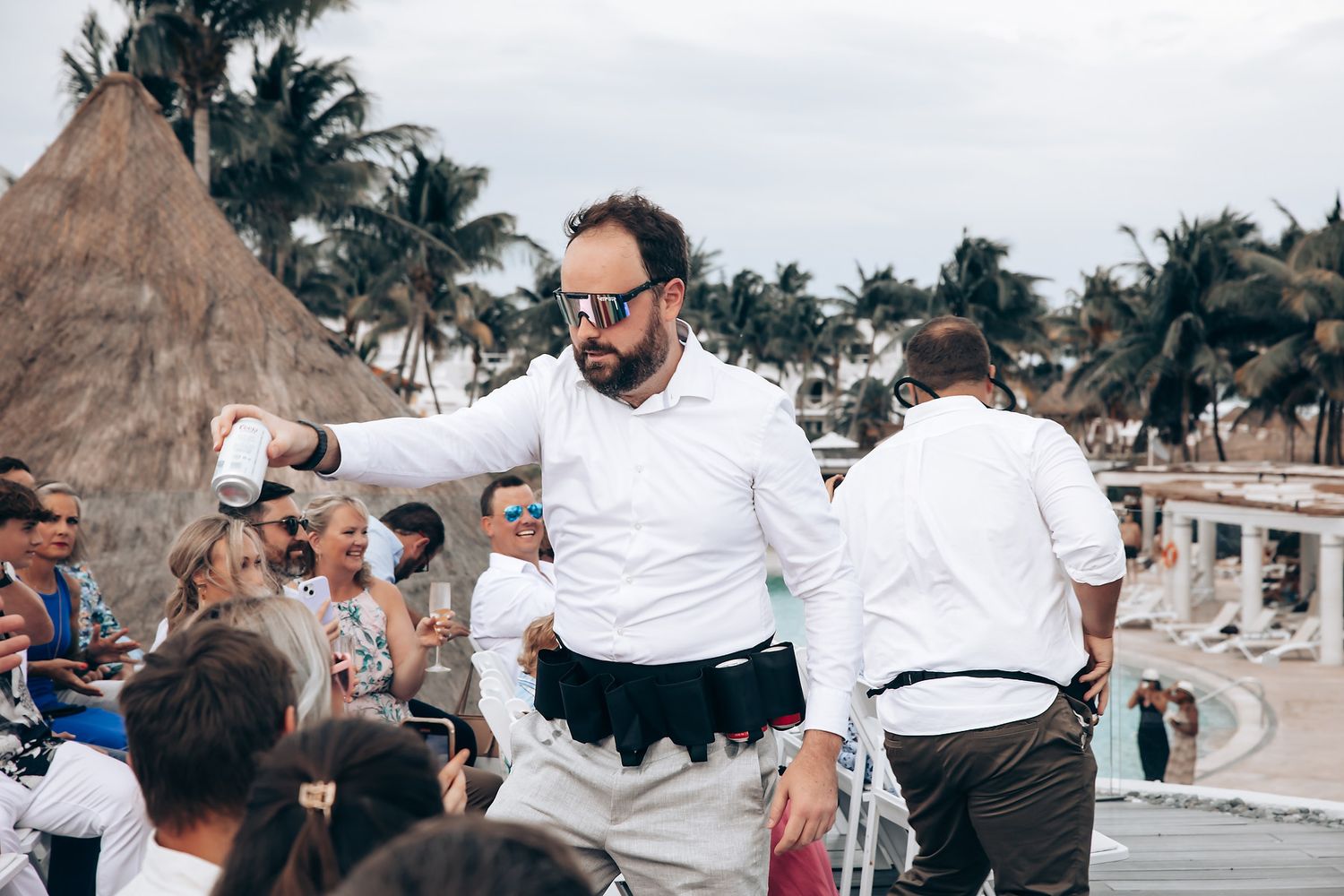 Wedding party in white attire celebrating on a tropical beach with palm trees.