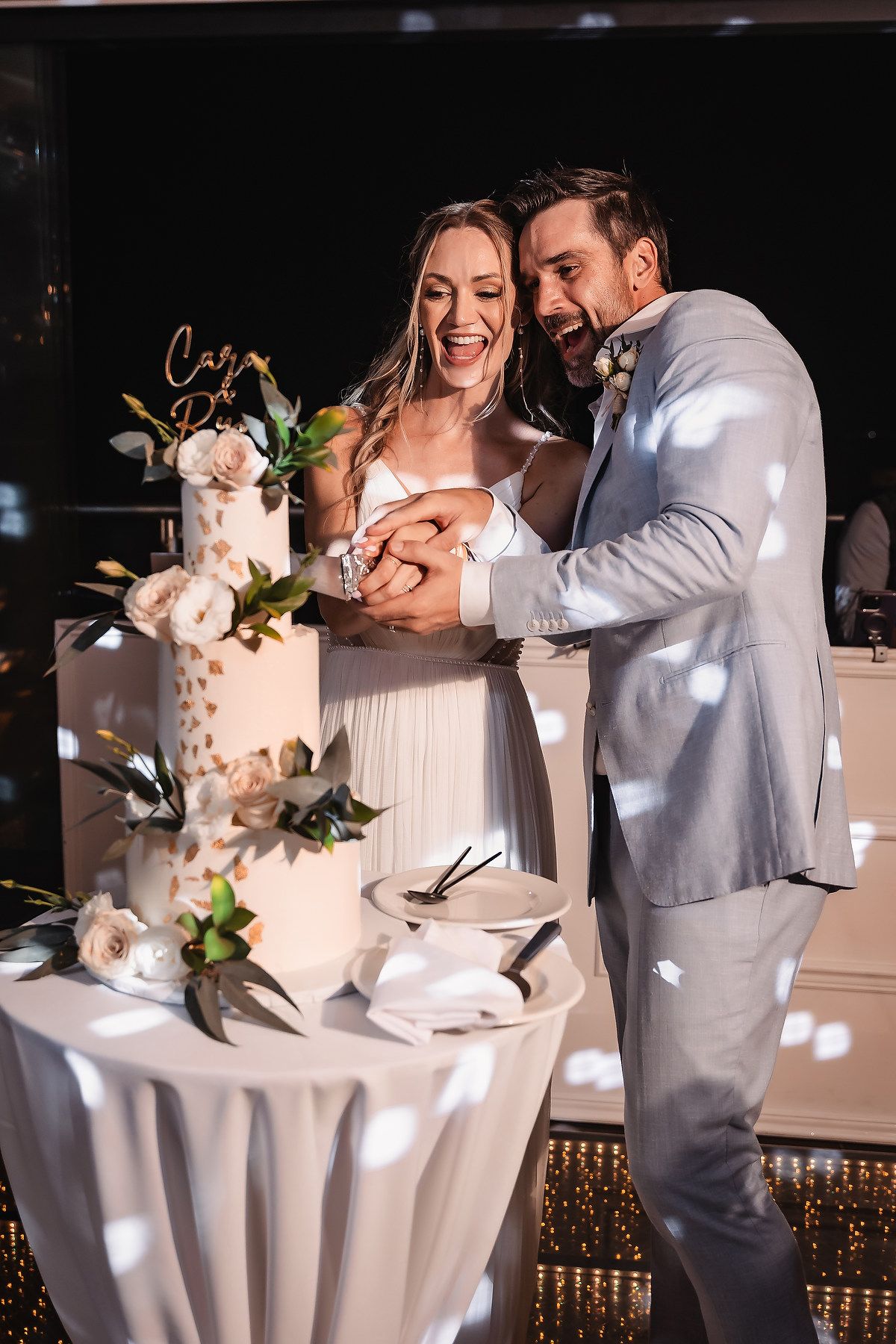 Wedding cake cutting moment at an elegantly decorated reception table with floral details.