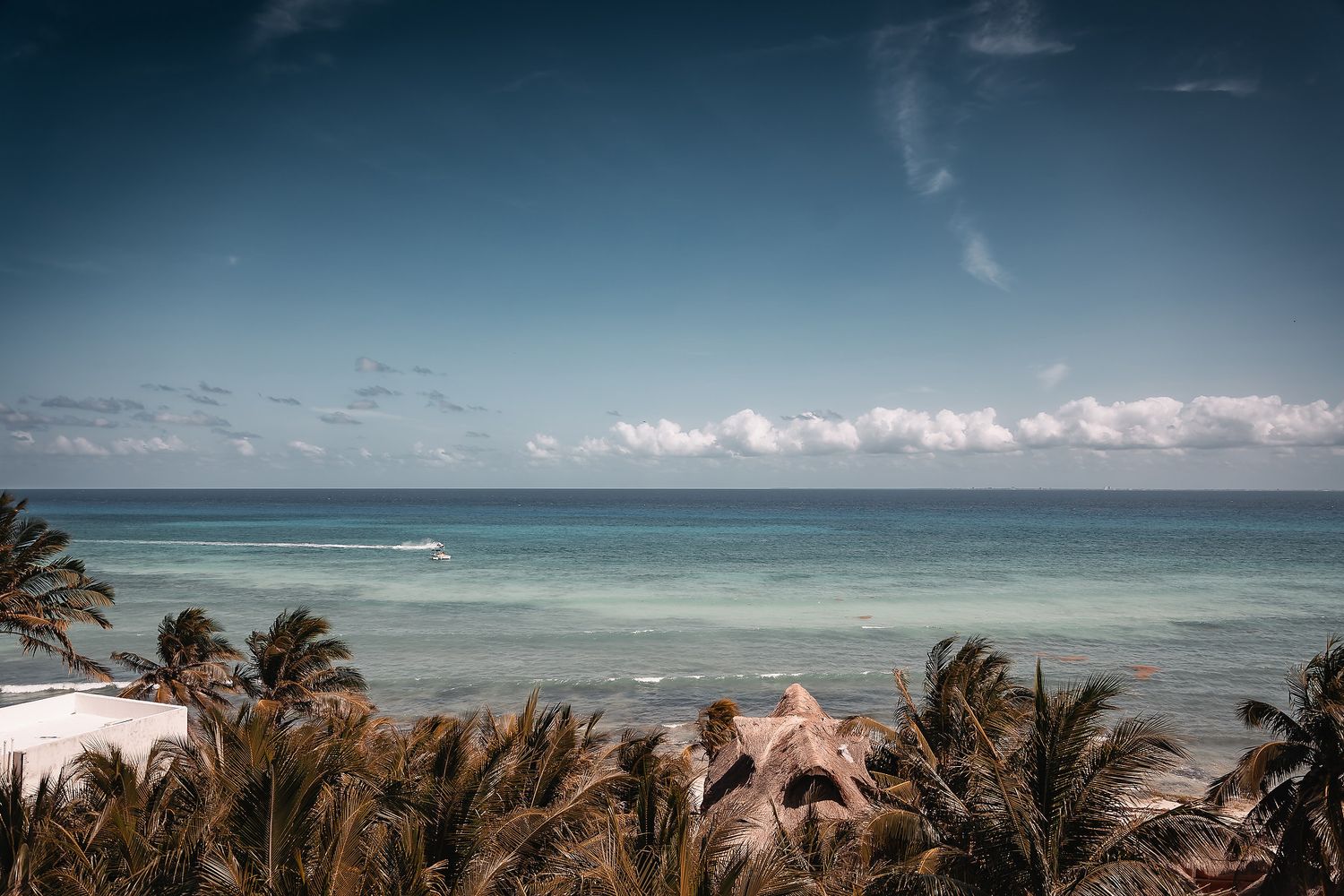 Panoramic view of a tropical beach coastline with turquoise waters and cloudy blue skies.