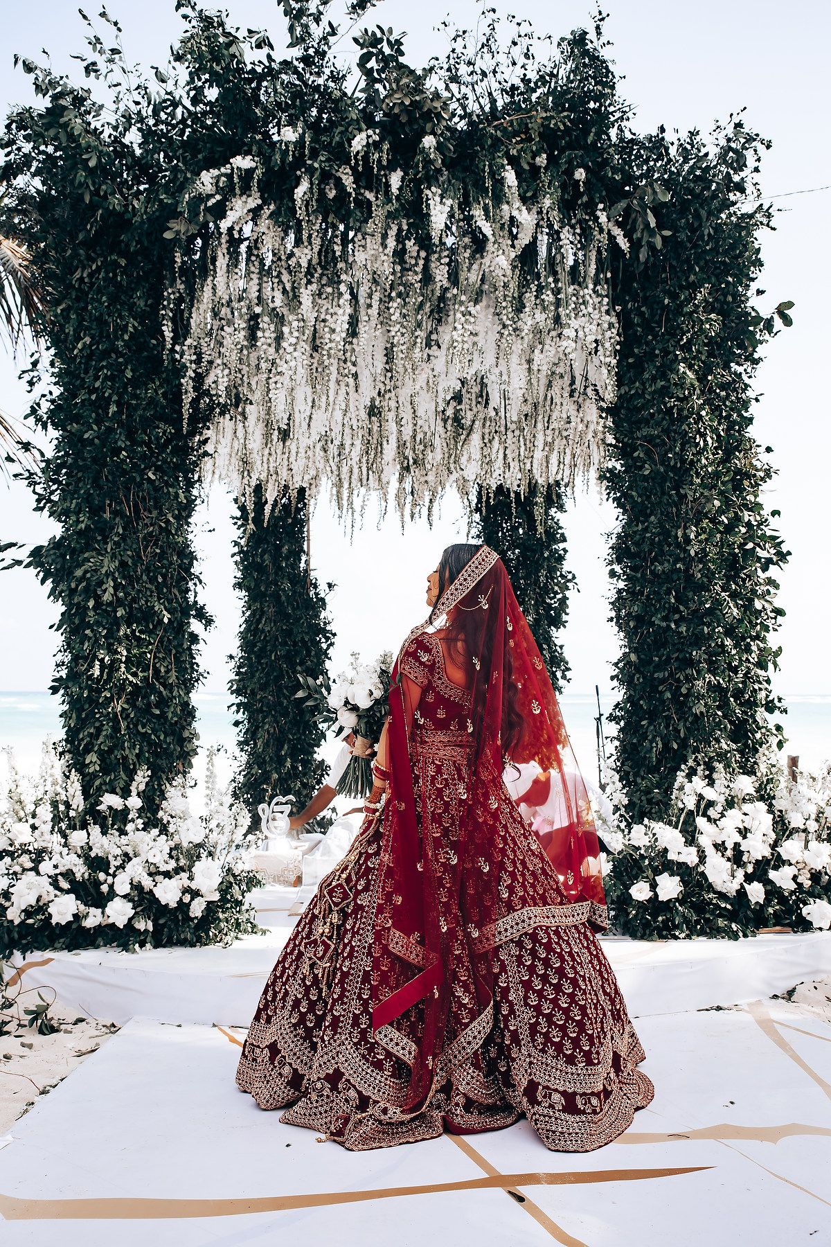 Traditional Indian wedding ceremony setup with red lehenga and floral decorations on a beach.