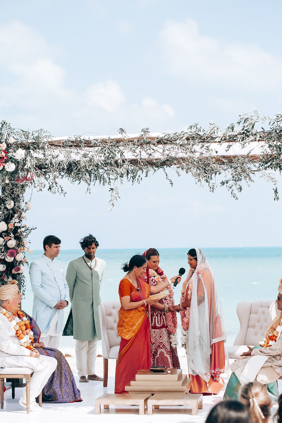 Traditional Indian wedding ceremony taking place under decorated mandap with ocean backdrop.