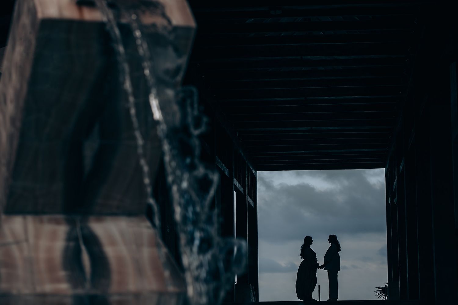 Silhouettes of two people framed in a dark doorway against a cloudy sky.