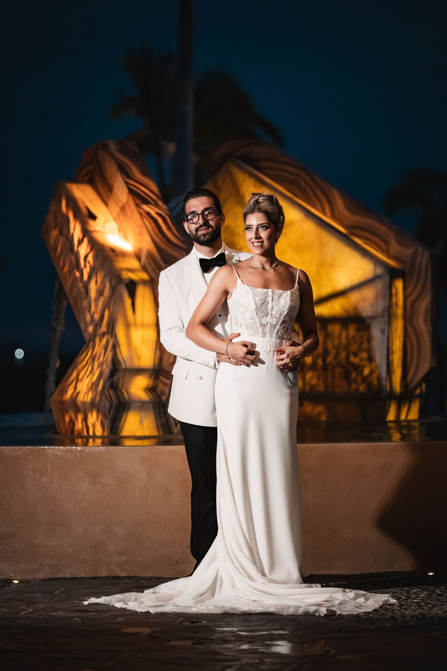 Romantic night wedding portrait with dramatic amber lighting against a dark background.