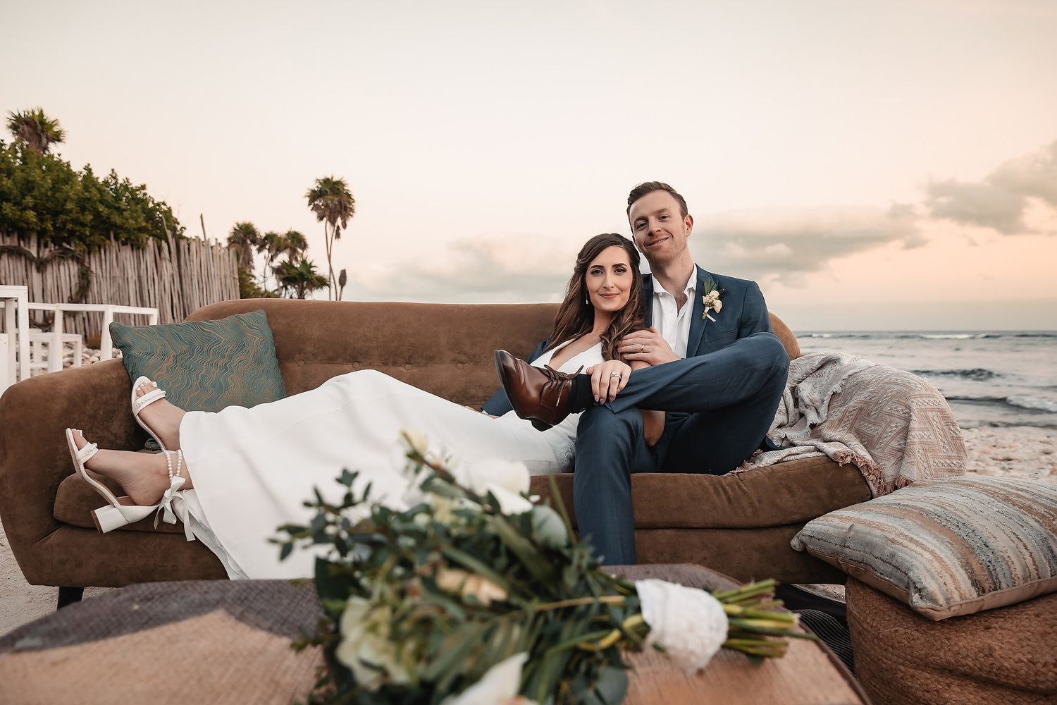 Wedding couple shares intimate moments on a brown leather couch by the ocean at sunset.