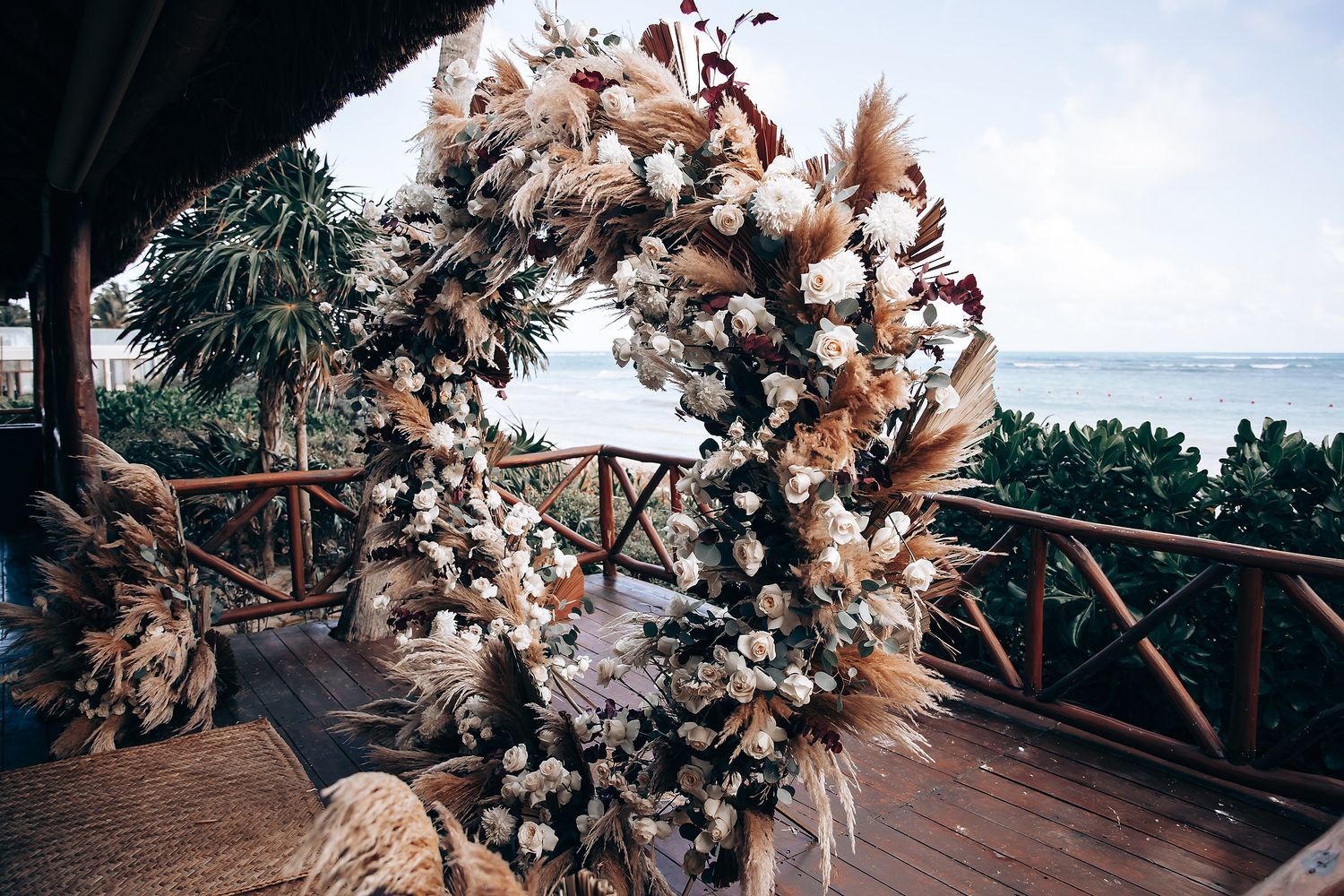 Elegant floral arrangements with dried pampas grass and white flowers decorating a beach venue.