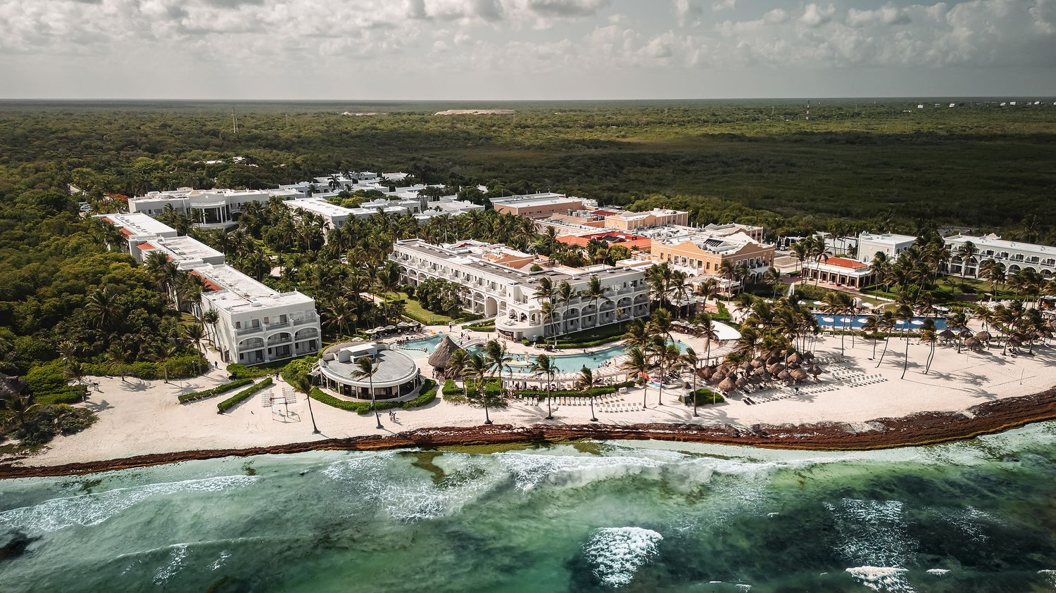 Aerial view of coastal resort properties and pristine beach along turquoise waters.