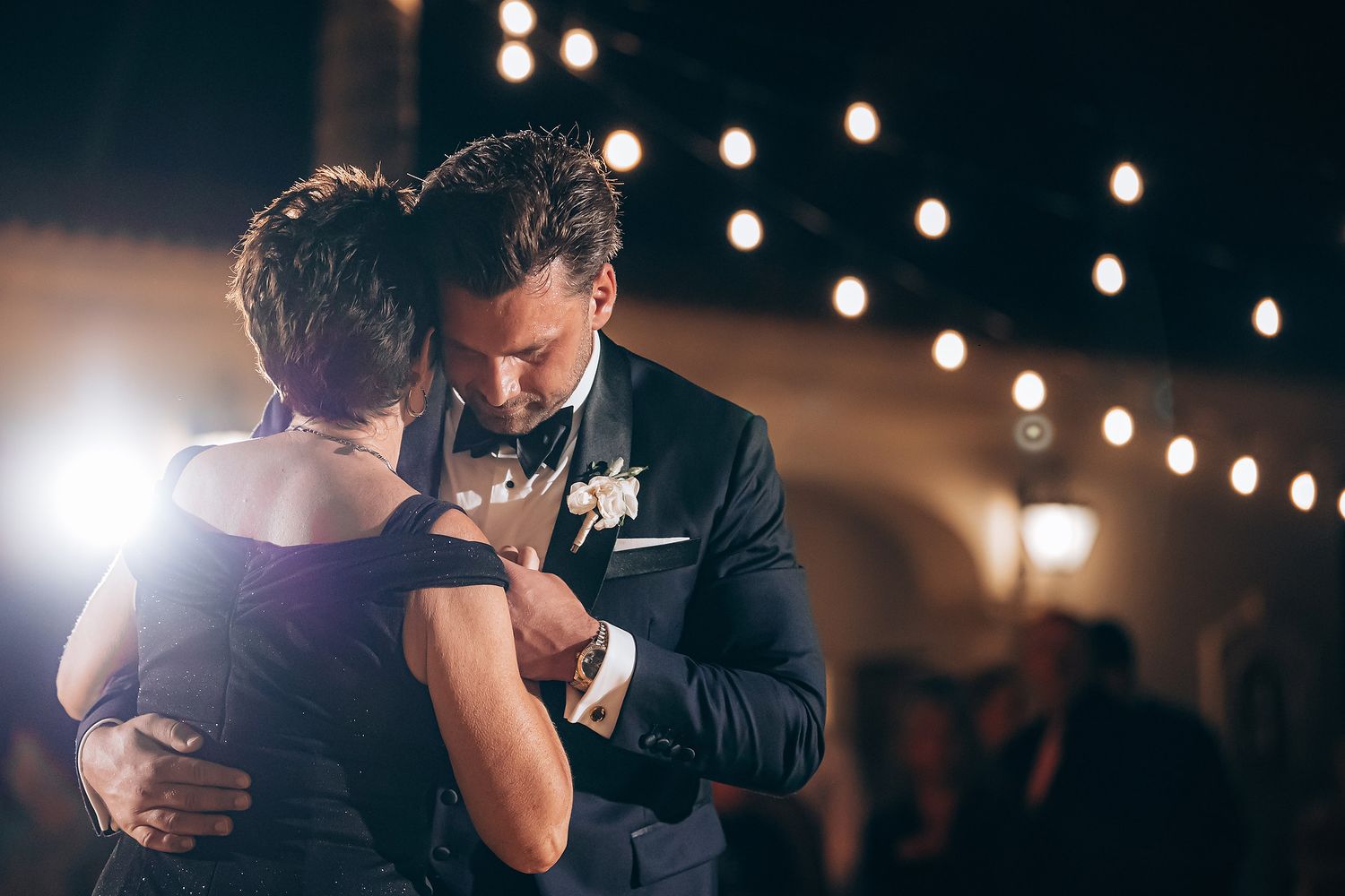 Couple shares intimate slow dance moment under twinkling lights at evening reception.