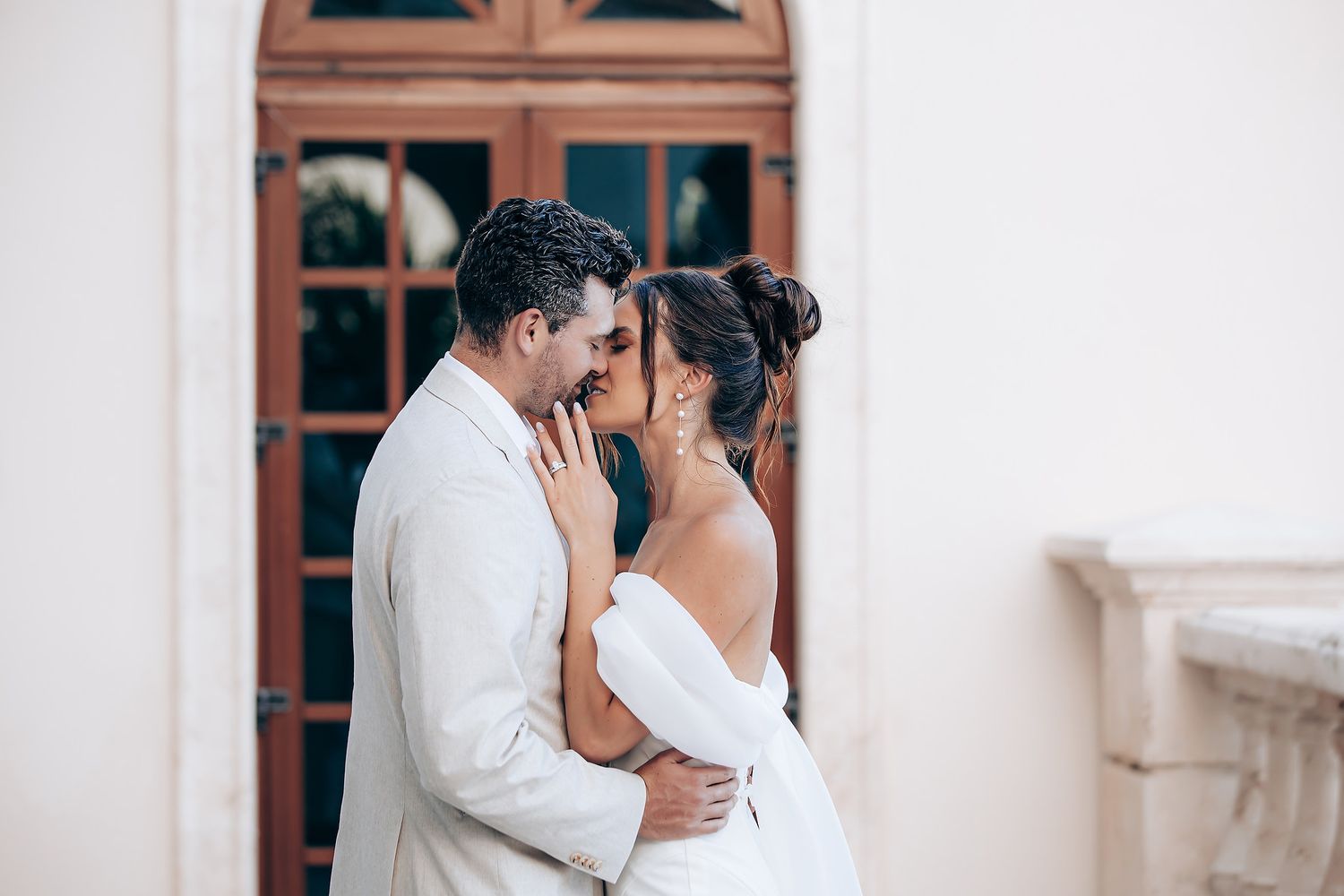 Elegant couple shares intimate moment in front of rustic wooden doors and white walls.