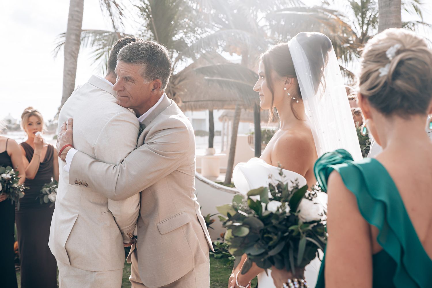 An emotional moment at a beach wedding ceremony as a couple embraces while guests look on in the background.
