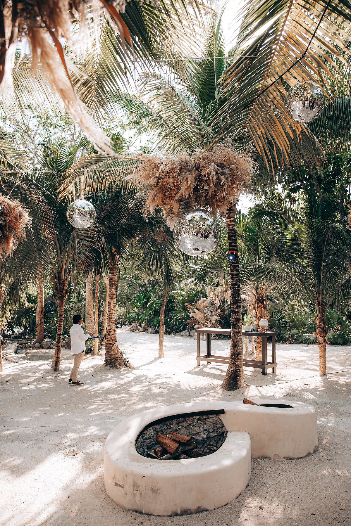 Palm trees line a sandy beach path with circular white stone seating areas creating a tranquil tropical atmosphere.